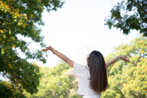 Portrait of teenage girl raising arms and laughing in the park.